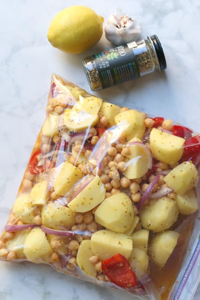 Ingredientes marinando en una bolsa grande con cremallera con un limón, una cabeza de ajo y un frasco de orégano seco al lado.