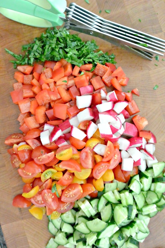 Perejil picado, tomates, rábanos, pimientos y pepinos en una tabla para cortar