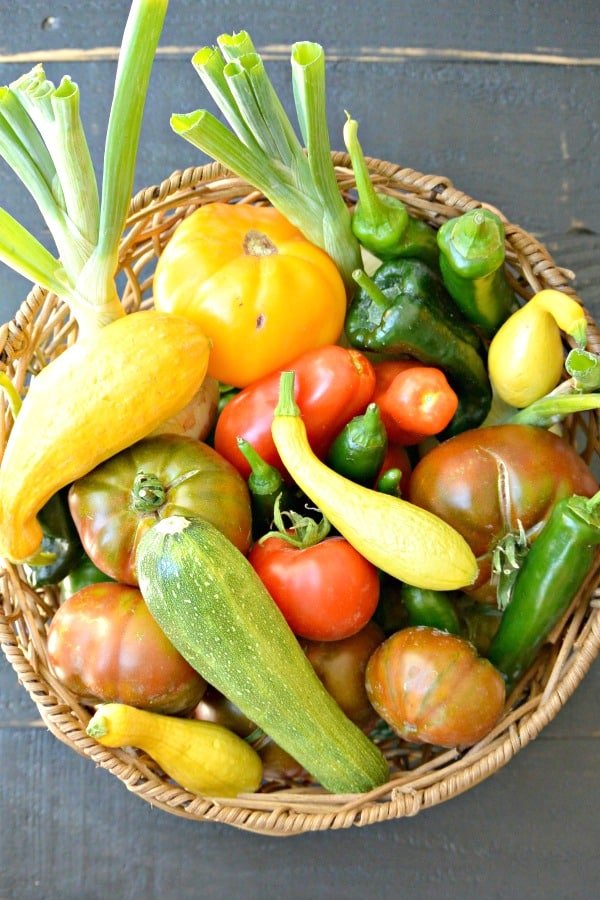 Canasta de productos que incluye calabazas de verano, cebollas, pimientos y tomates tradicionales en diferentes colores
