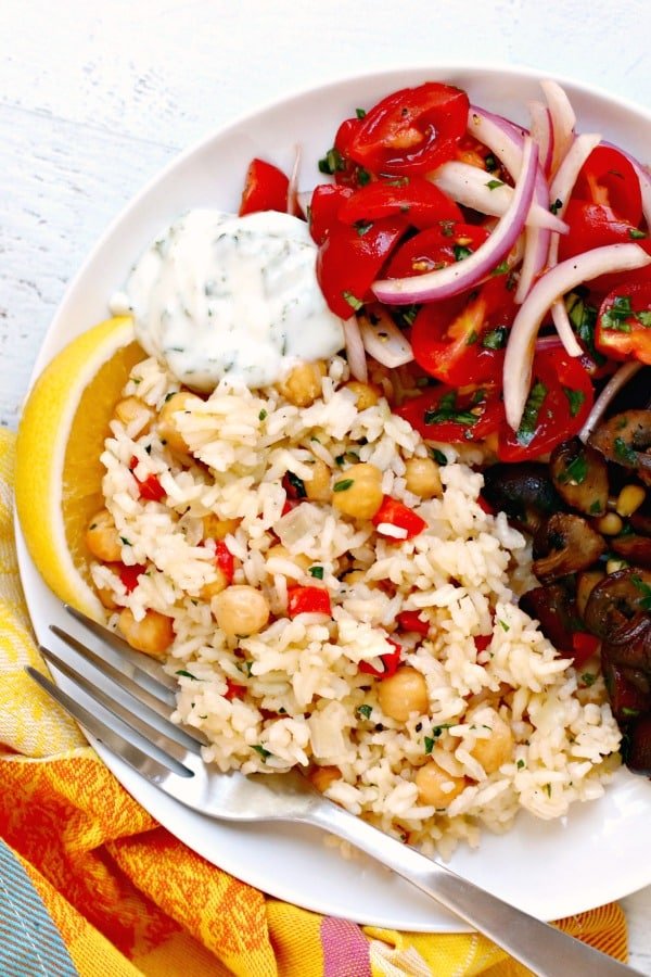 Plato con arroz pilaf, champiñones asados, ensalada de tomate y cebolla y una cucharada de salsa con un tenedor y una rodaja de limón