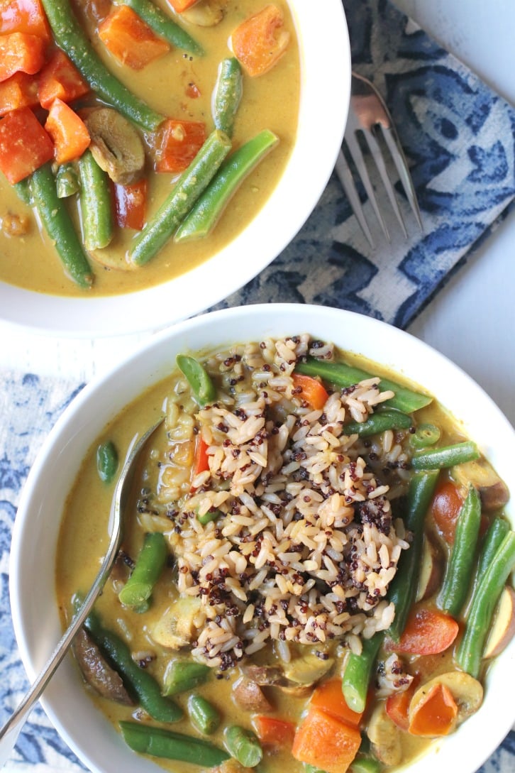 Cerca de dos tazones de curry de judías verdes, uno con un tenedor y arroz integral y quinoa