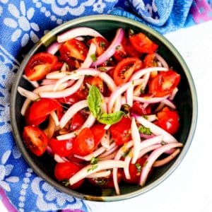 Tazón de ensalada de tomate y cebolla adornada con una ramita de albahaca fresca