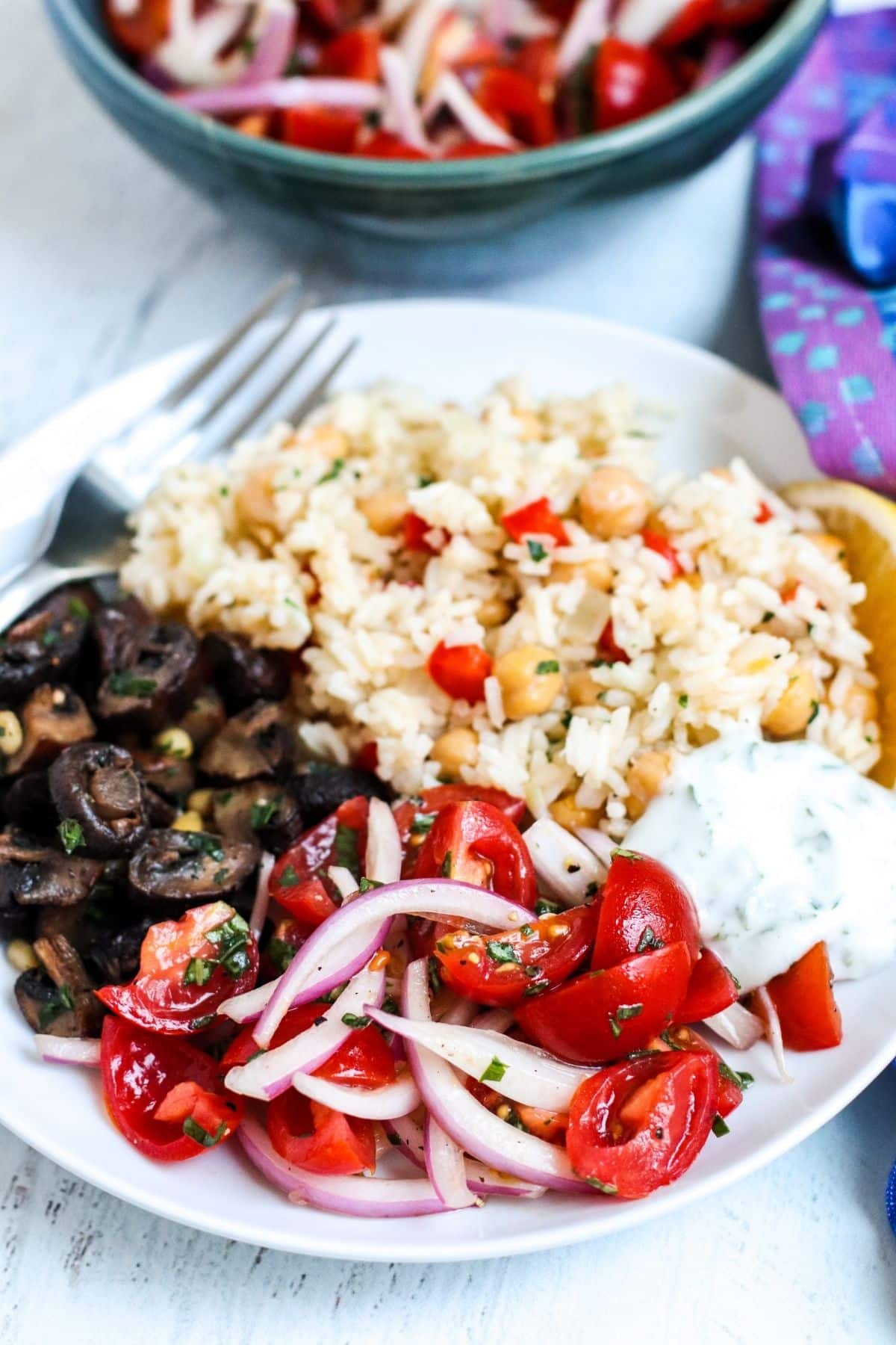 Plato llano con arroz pilaf de garbanzos, salsa de yogur, ensalada de tomate y cebolla y champiñones asados