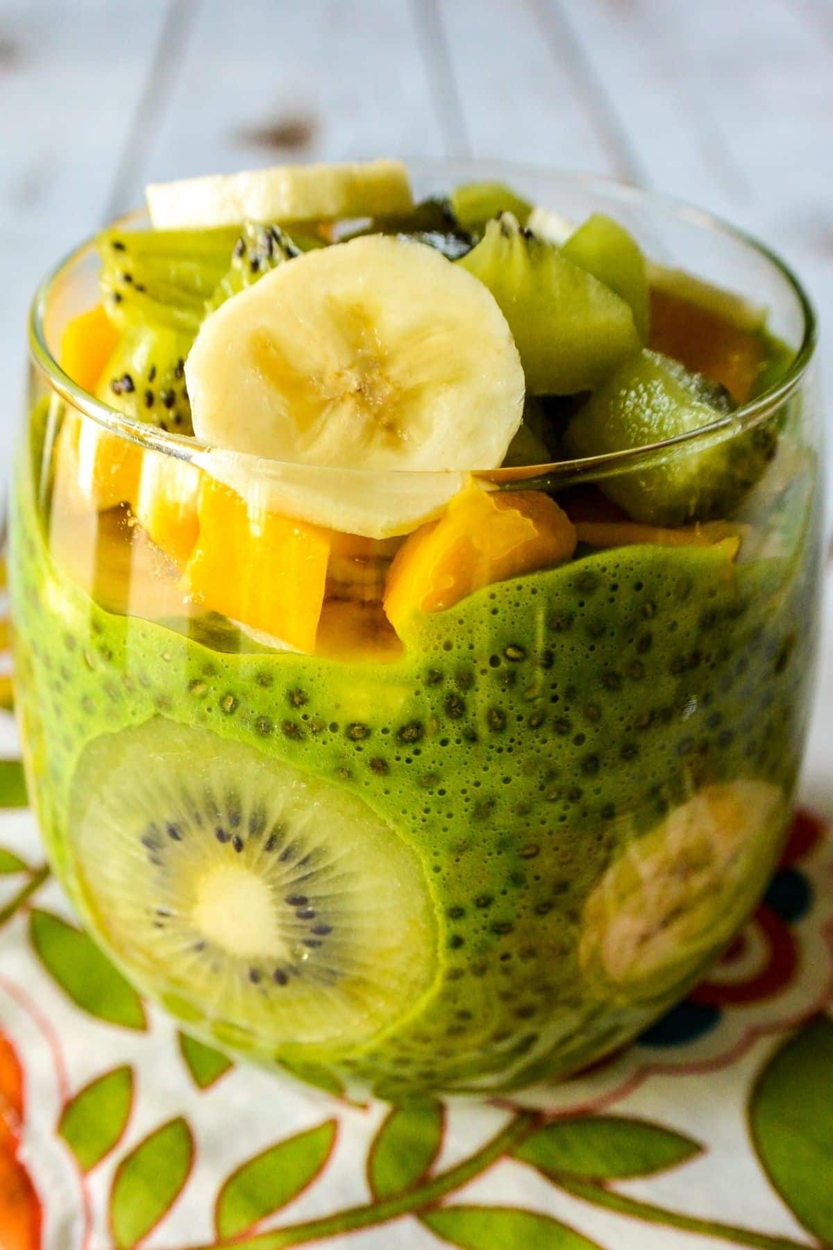 Budín de semillas de chía verde en un vaso transparente cubierto con rodajas de kiwi, mango y plátano